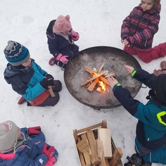 Kinder sitzen im Schnee um eine Feuerschale